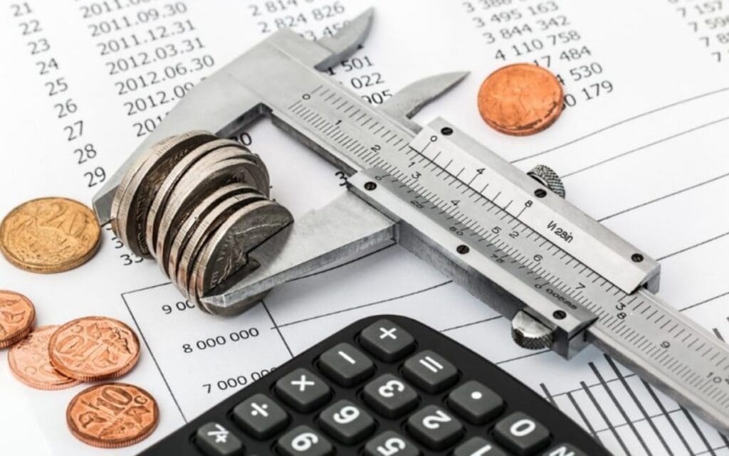 A calculator, coins and ruler on top of some papers