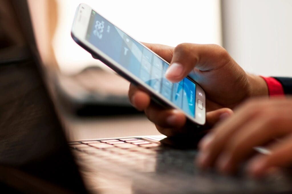 A person is holding their phone and typing on the keyboard.