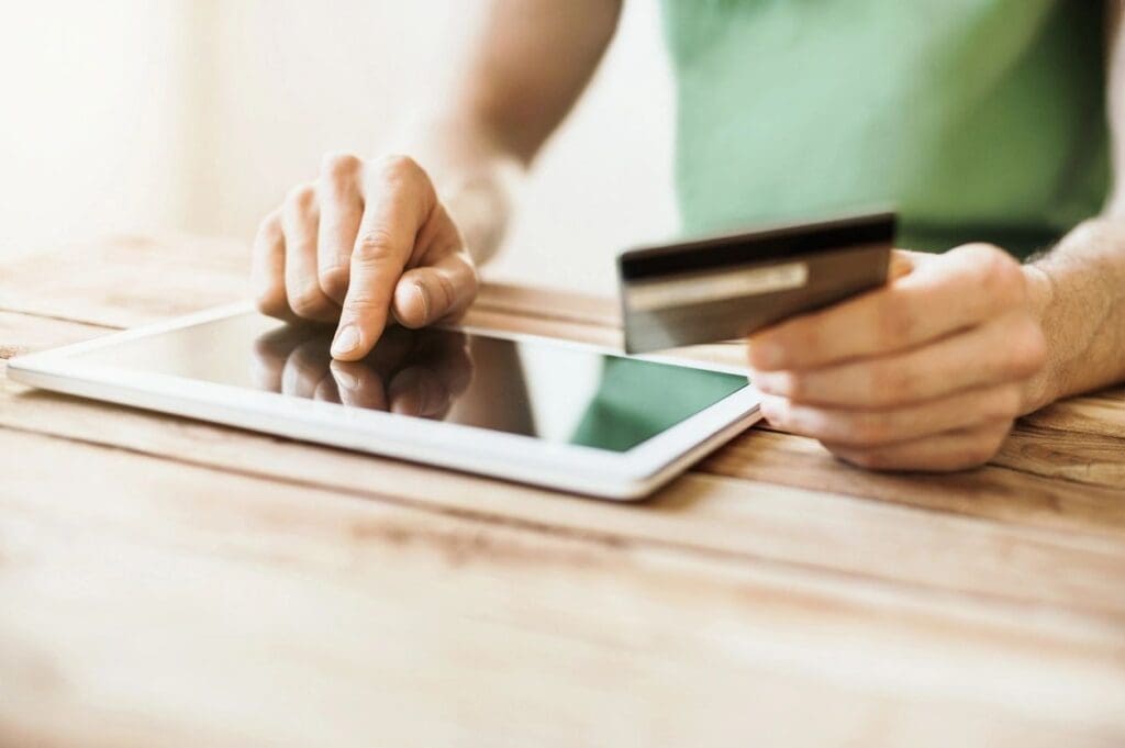 A person holding a credit card and using a tablet.