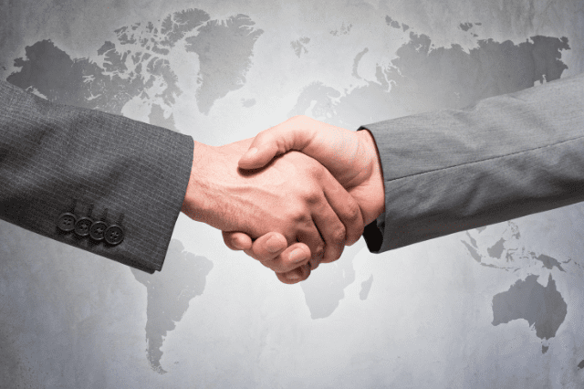 Two people shaking hands in front of a world map.
