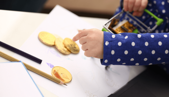 A child 's hand pointing to some gold coins.