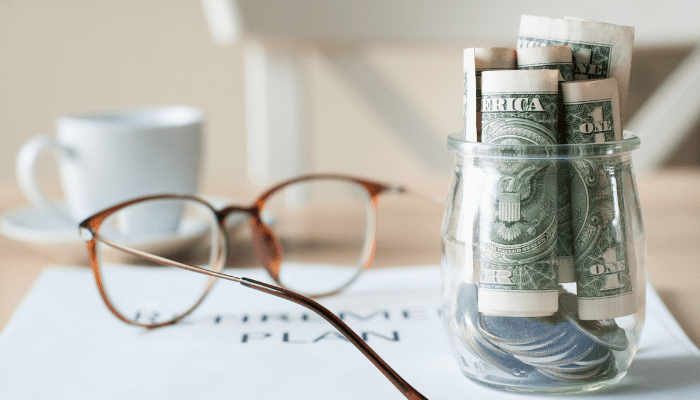 A glass jar with money in it and glasses.