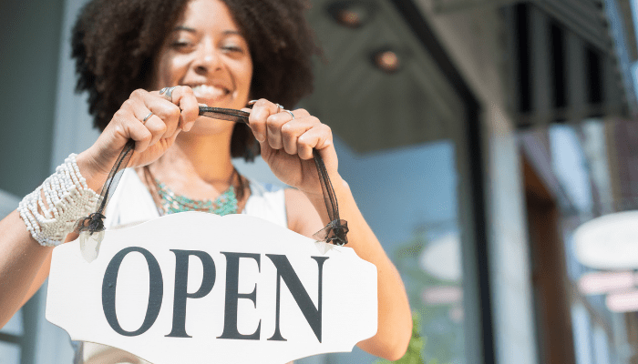 A woman holding an open sign outside of a store.