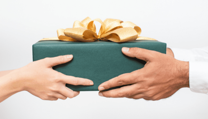 Two hands holding a green gift box with gold bow.