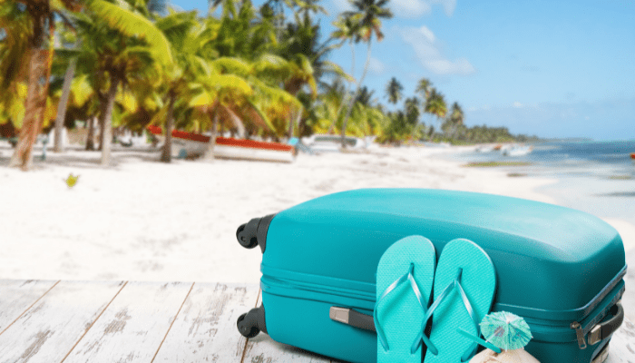 A blue suitcase and flip flops on the beach.