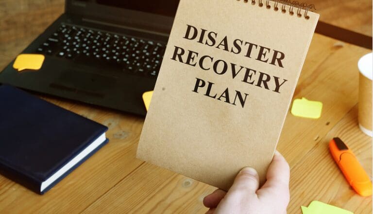 A person holding up a paper with the words disaster recovery plan written on it.