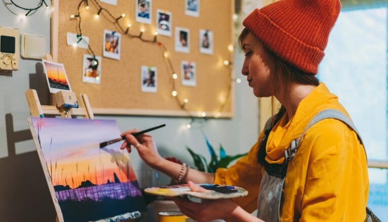 A woman painting with a paintbrush and a canvas.