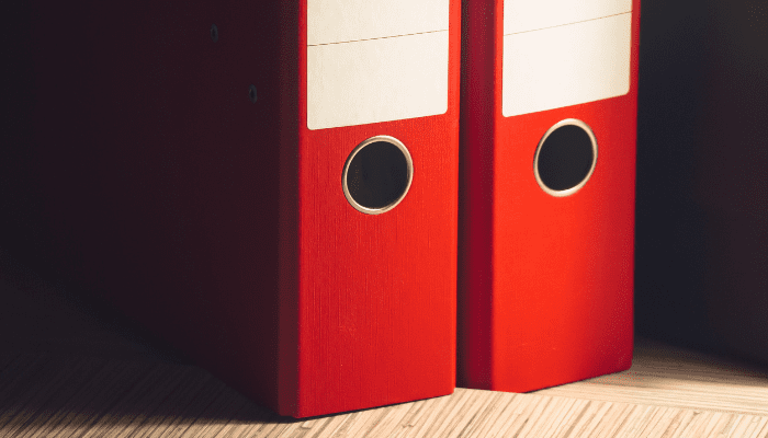 Two red binders on a wooden surface.